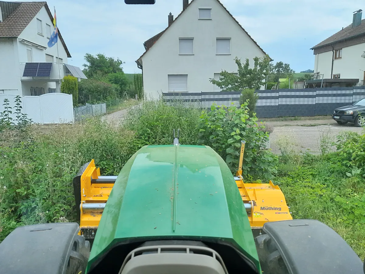 Schlegelmulcher am Schlepper vor einem zugewachsenen Grundstück